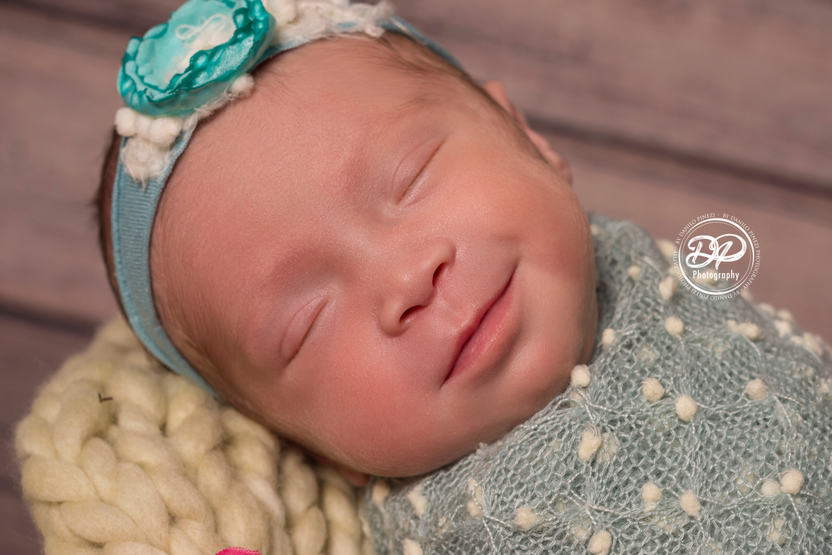Bebê recém nascida sorrindo, dormindo tranquilamente enrolada em wrap pipoca, em sessão newborn realizada no Estúdio Danilo Pinezi Fotografia em Bariri