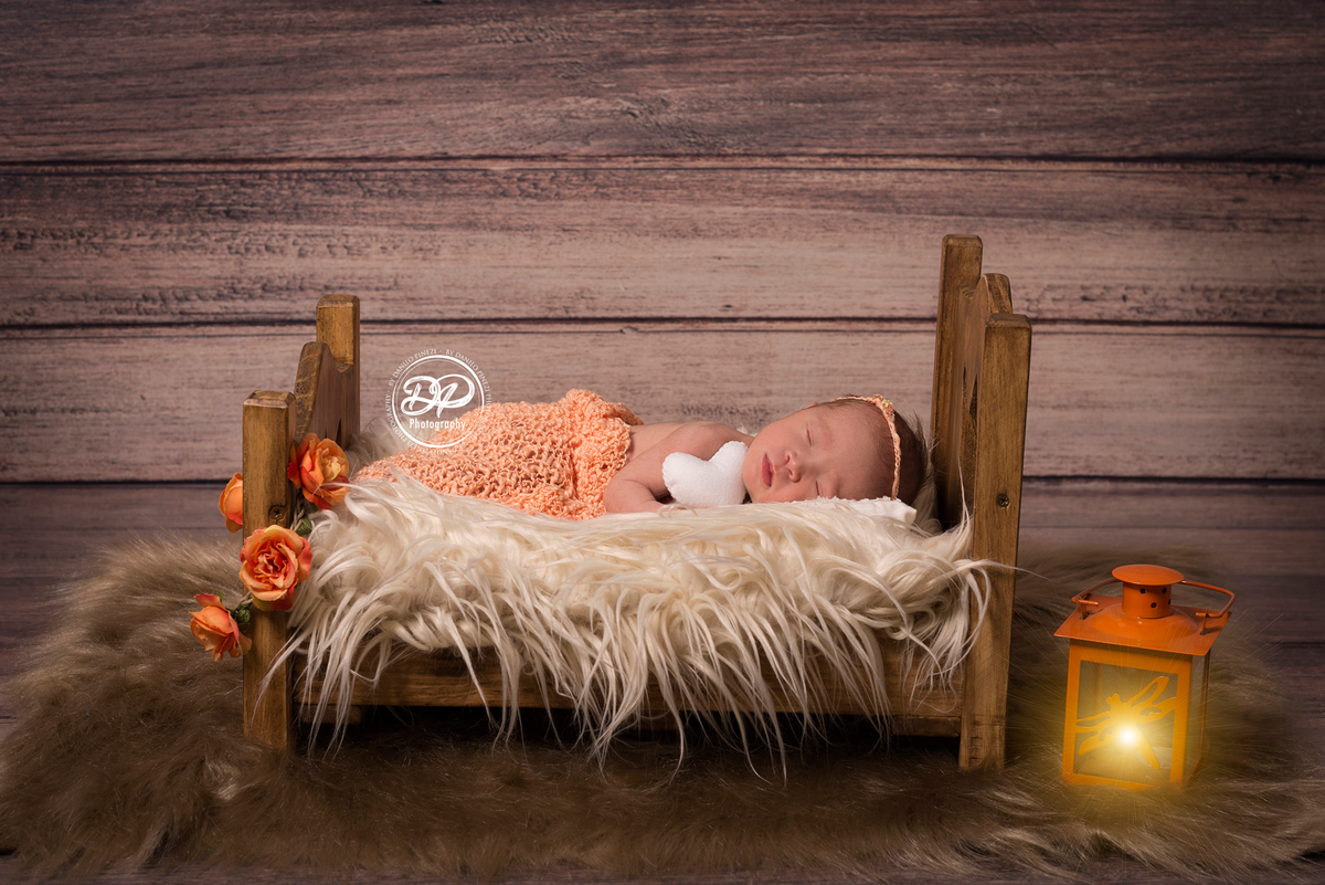 Bebê recém nascida vestida de anjo, deitada em uma caminha segurando um coração, dormindo tranquilamente em sessão newborn realizada no Estúdio Danilo Pinezi Fotografia em Bariri