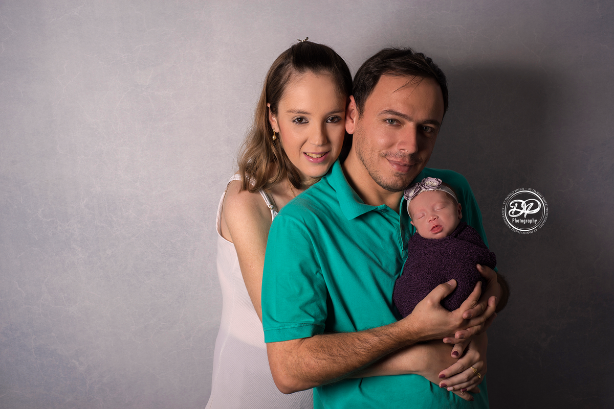 Pais segurando sua filha recém nascida nos braços, em uma sessão newborn no estúdio Danilo Pinezi Fotografia em Bariri