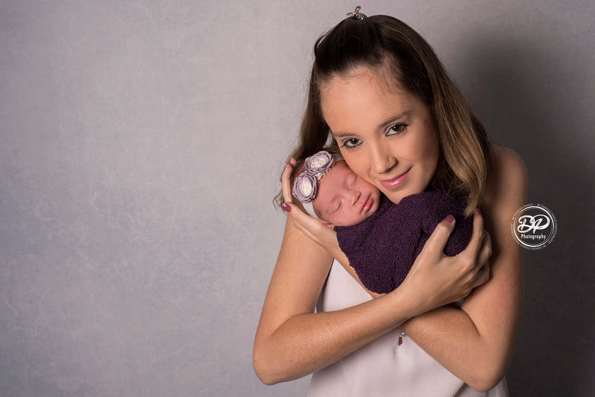 mamãe segurando sua filha recém nascida nos braços, em uma sessão newborn no estúdio Danilo Pinezi Fotografia em Bariri