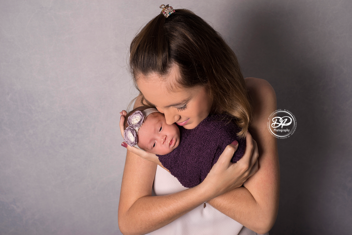 mamãe segurando sua filha recém nascida nos braços, em uma sessão newborn no estúdio Danilo Pinezi Fotografia em Bariri
