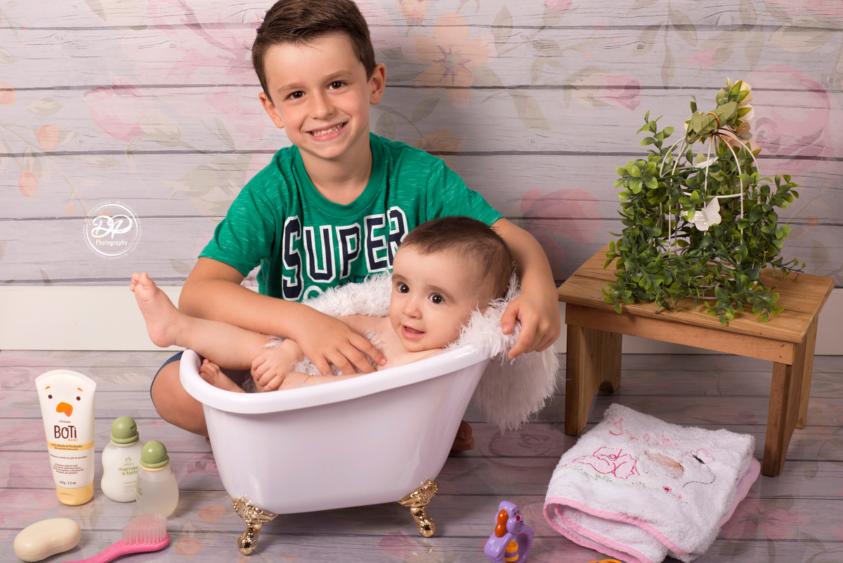 Ensaio de Menina, tomando banho em uma banheira, com touca de banho rosa, com seu irmão mais velho, em um fundo de madeira com flores, executado pelo fotógrafo profissional Danilo Pinezi em Bariri