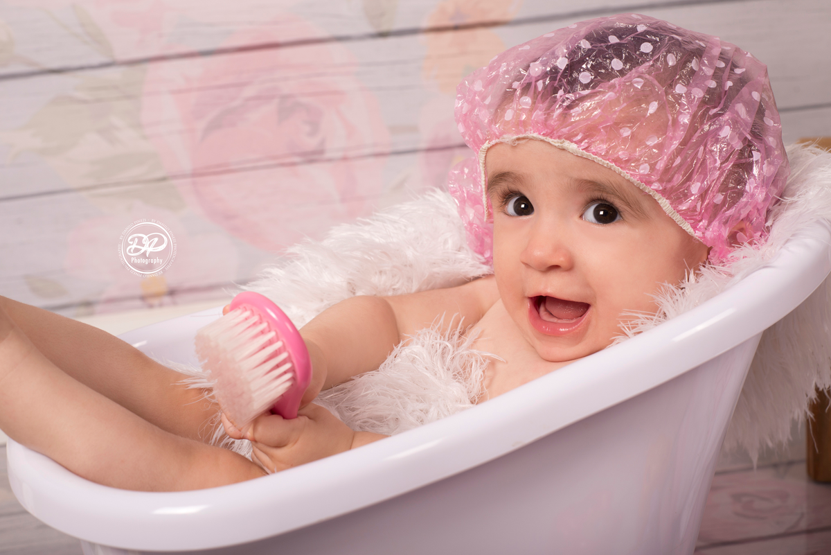 Ensaio de Menina, tomando banho em uma banheira, com touca de banho rosa, em um fundo de madeira com flores, executado pelo fotógrafo profissional Danilo Pinezi em Bariri