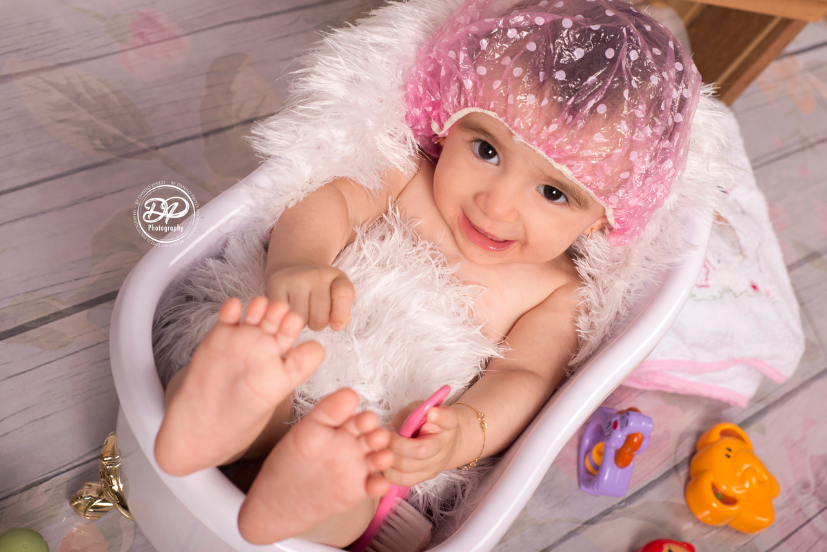 Ensaio de Menina, tomando banho em uma banheira, com touca de banho rosa, em um fundo de madeira com flores, executado pelo fotógrafo profissional Danilo Pinezi em Bariri