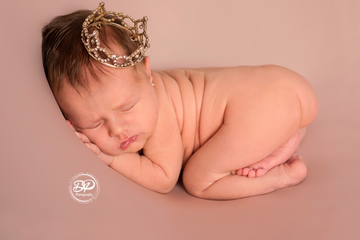 Newborn de menina executado em Bariri, pose do bumbum com coroa na cabeça no puff de fundo rosé, estúdio Danilo Pinezi Fotografia