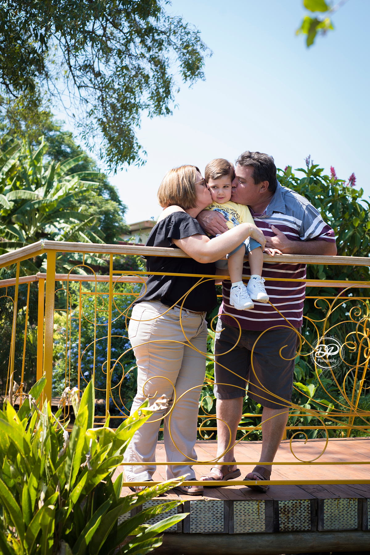 Avós beijando o neto numa ponte de jardim, em ensaio família  externo feito em bariri/ SP.