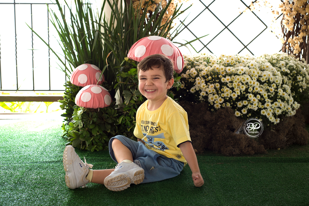 Menino sentado sorrindo em meio a cogumelos,  em ensaio família realizado em Bariri/SP