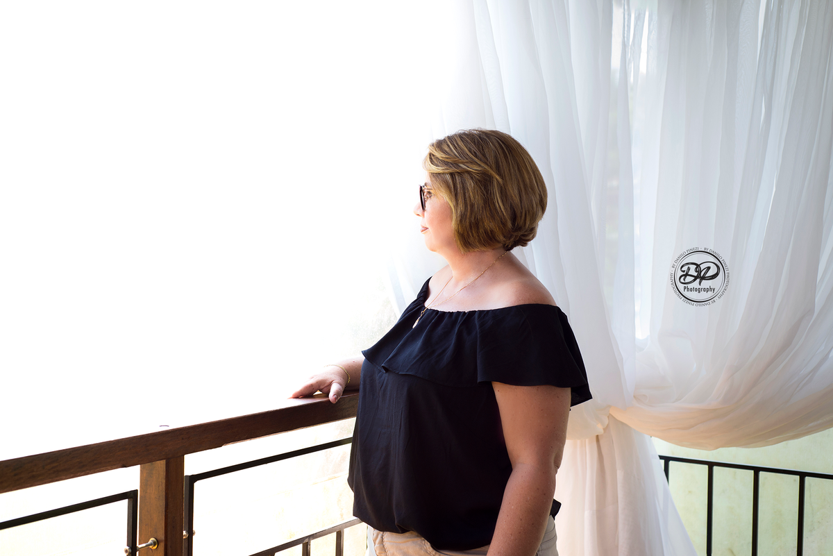 Mulher olhando por uma sacada com cortinas brancas, em ensaio família feito em Bariri SP