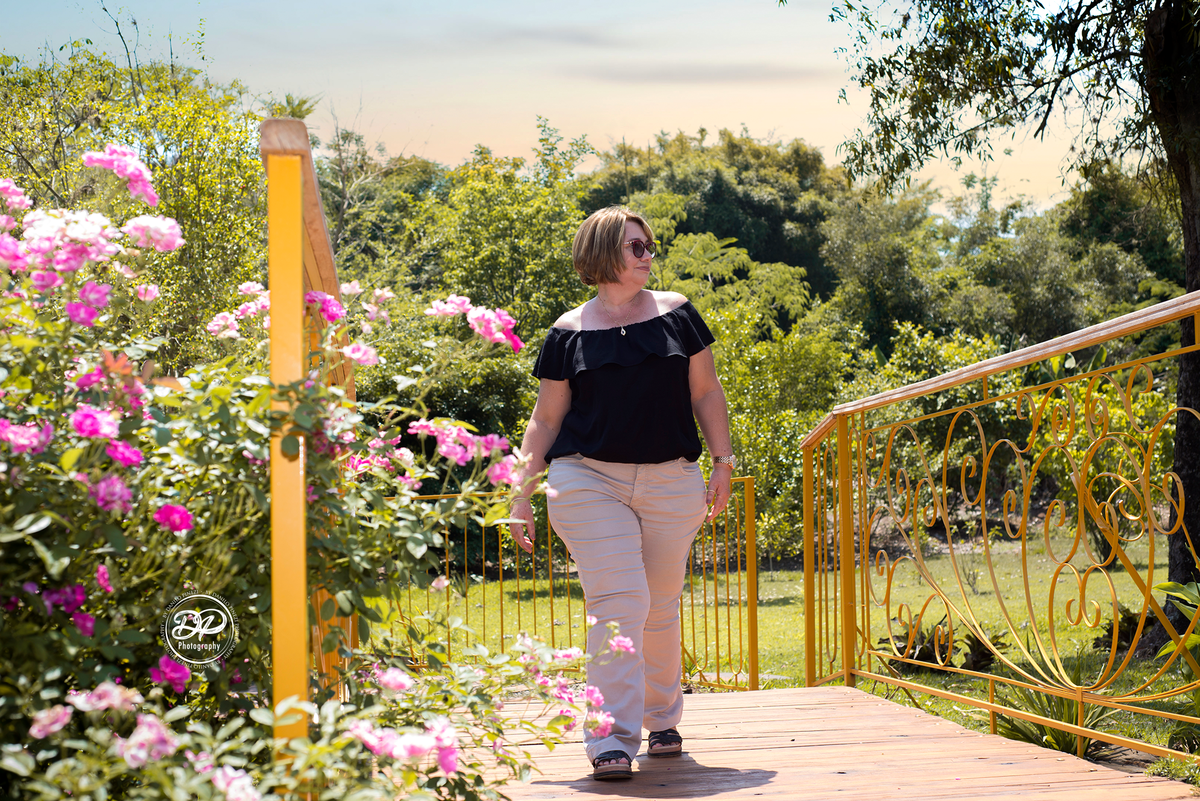 Mulher caminhando por uma ponte cheia de flores em jardim, em ensaio família feito em Bariri SP