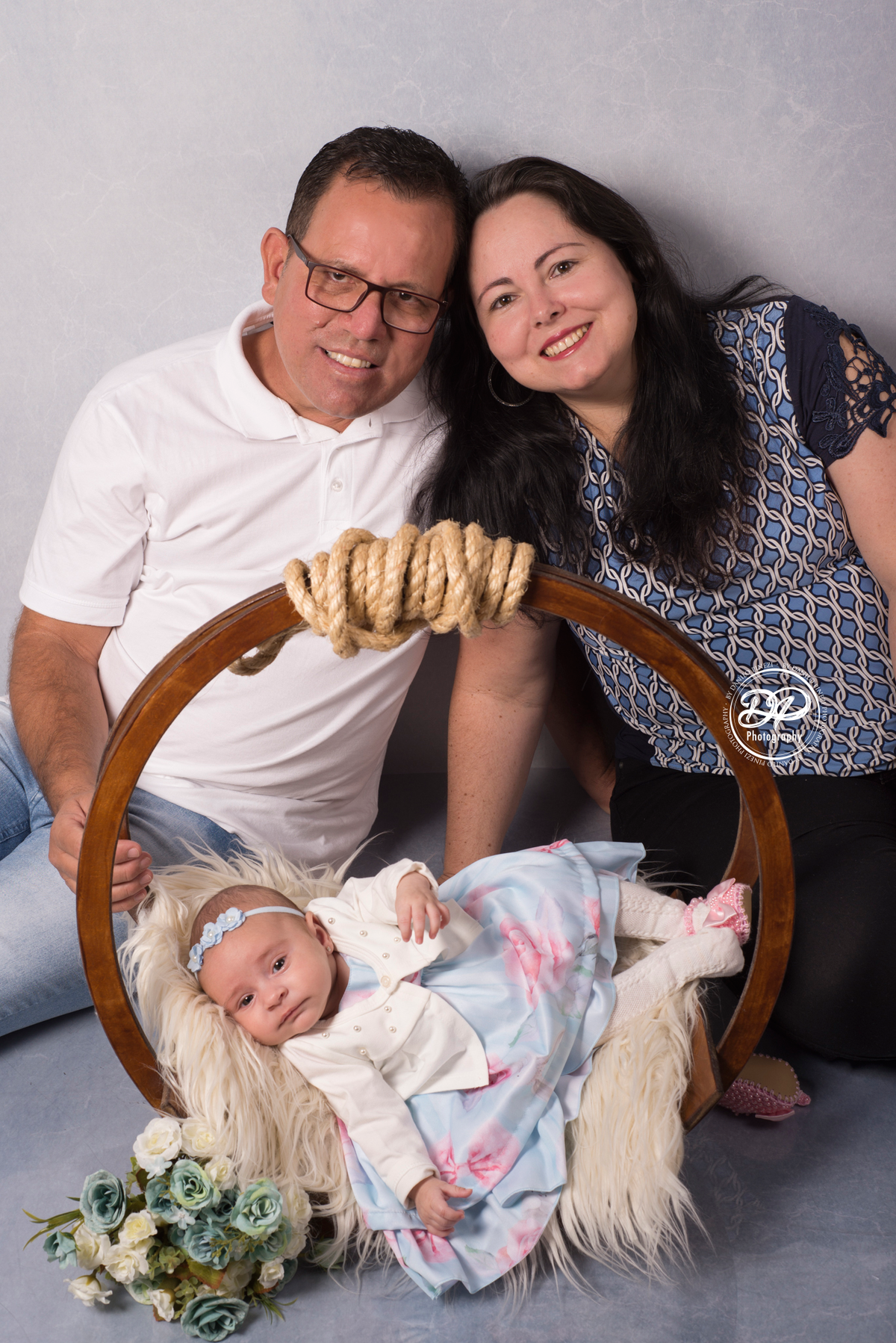 Sessão de 2 meses de bebê menina deitada em balanço circular rústico, adornado com flores e água de cheiro, em sessão realizada no estúdio Danilo Pinezi Fotografia. Fotos com os pais