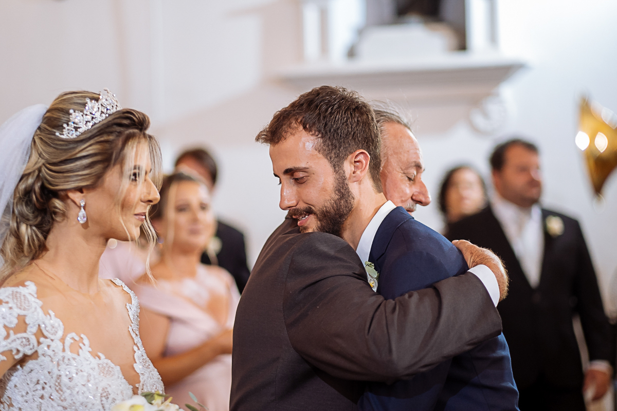 registro fotográfico do casamento de Flávia e Johnn, em Vitória-ES, por Schmitz Fotografia, fotógrafos de casamento no Espírito Santo,pai da noiva abraçando o noivo