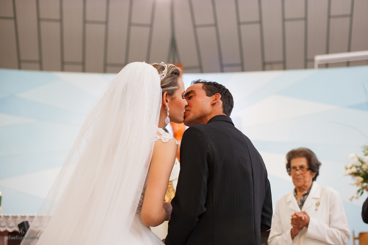 enfim casados, o beijo tão esperado, moradores, padrinhos, pais e amigos ficam em pé para comemorar esta linda união