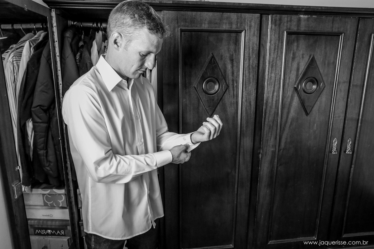 jaque risse, andre risse, estudio bebedouro, melhores fotografos, making of do noivo onde ele está abotoando a manga da camisa em frente a um guarda roupa