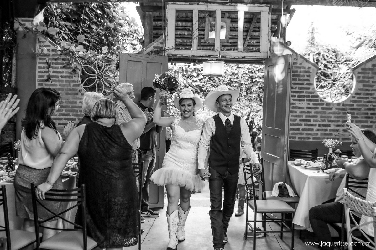 jaque risse, andre risse, estudio bebedouro, melhores fotografos, entrada super animada dos noivos no salão da festa ambos vestindo chapéus country