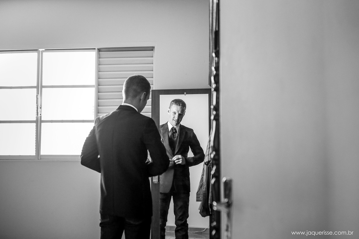 jaque risse, andre risse, estudio bebedouro, melhores fotografos, noivo se olhando no espelho terminando de abotoar o paletó durante o makin of