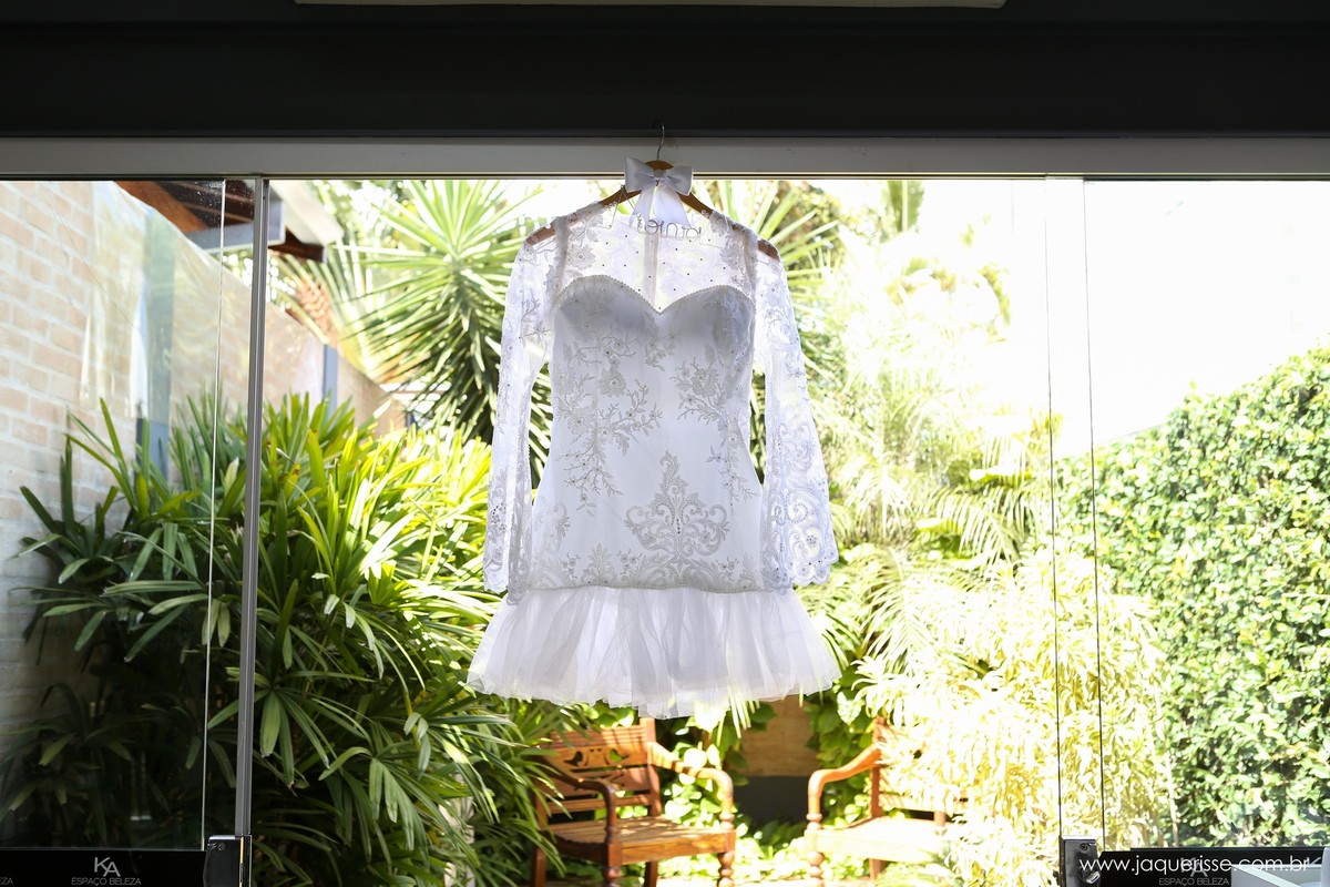 jaque risse, andre risse, estudio bebedouro, melhores fotografos, vestido curto e de mangas longas da noiva pendurado em uma porta aberta com muitas plantas ao fundo