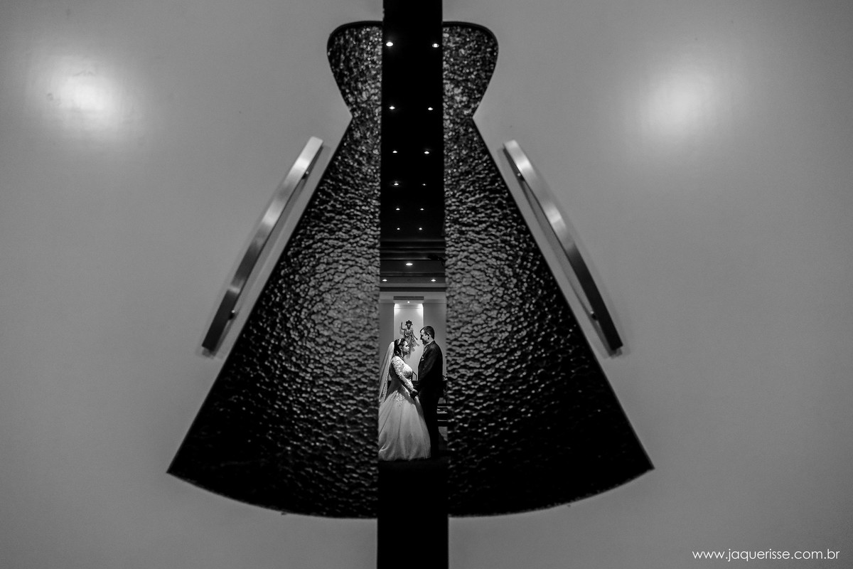 foto dos noivos vistos de uma fresta da porta da igreja que possui um vitral de nossa senhora aparecida no click da fotógrafa de casamento Bebedouro SP Jaque Risse