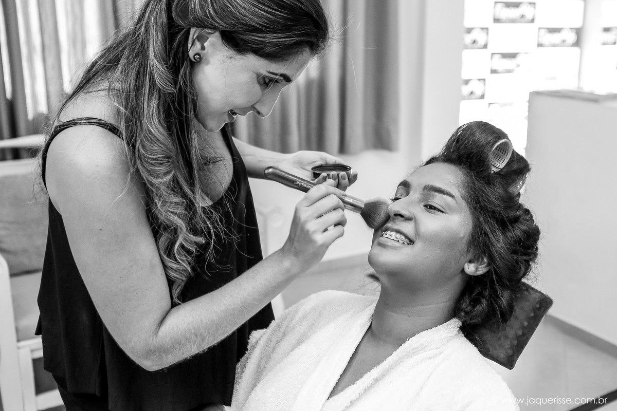 noiva sorridente com a maquiadora passando maquiagem em seu rosto no click da fotógrafa de casamento Bebedouro SP Jaque Risse