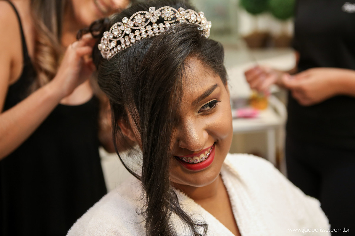 noiva com a franja do cabelo caida sobre um dos olhos e a cabeleireira terminando de colocar a coroa no click da fotógrafa de casamento Bebedouro SP Jaque Risse