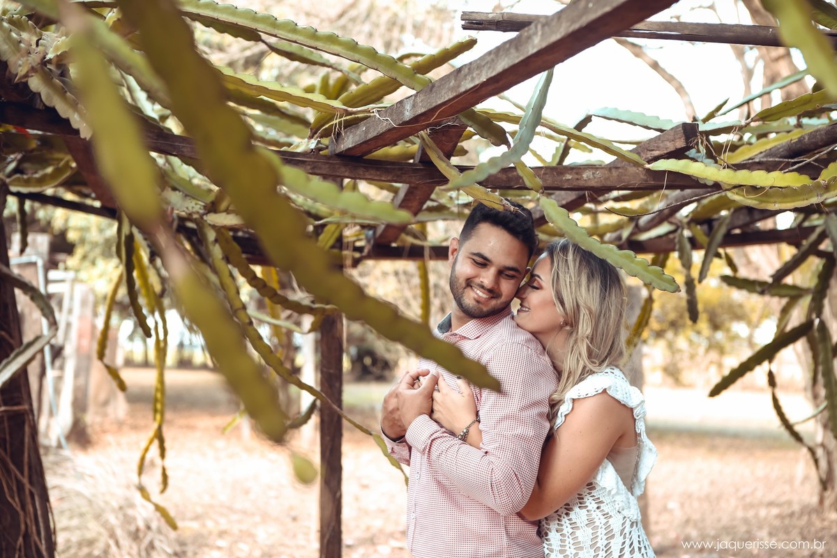 Noiva linda de vestido branco abraçando o noivo pelas costas e dando um suave beijo em sua orelha na cena do Pre wedding clicado pela fotografo de casamento jaque risse em bebedouro sp