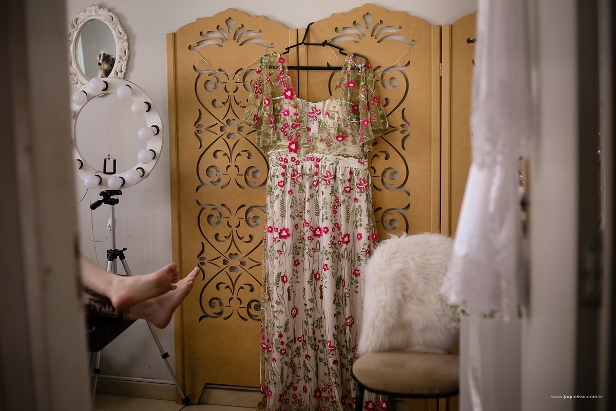 Lindo vestido florido da noiva pendurado em um cabide durante o making of clicado pela fotografa de casamento jaque risse em bebedouro SP