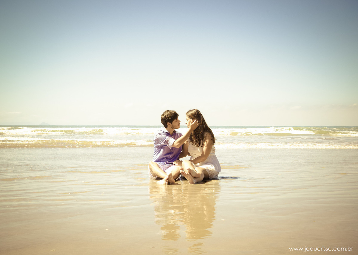 jaque risse, andre risse, estudio bebedouro, melhores fotografos, noivos sentados na areia da praia, noivo com a mao no rosto da noiva, ambos se olhando