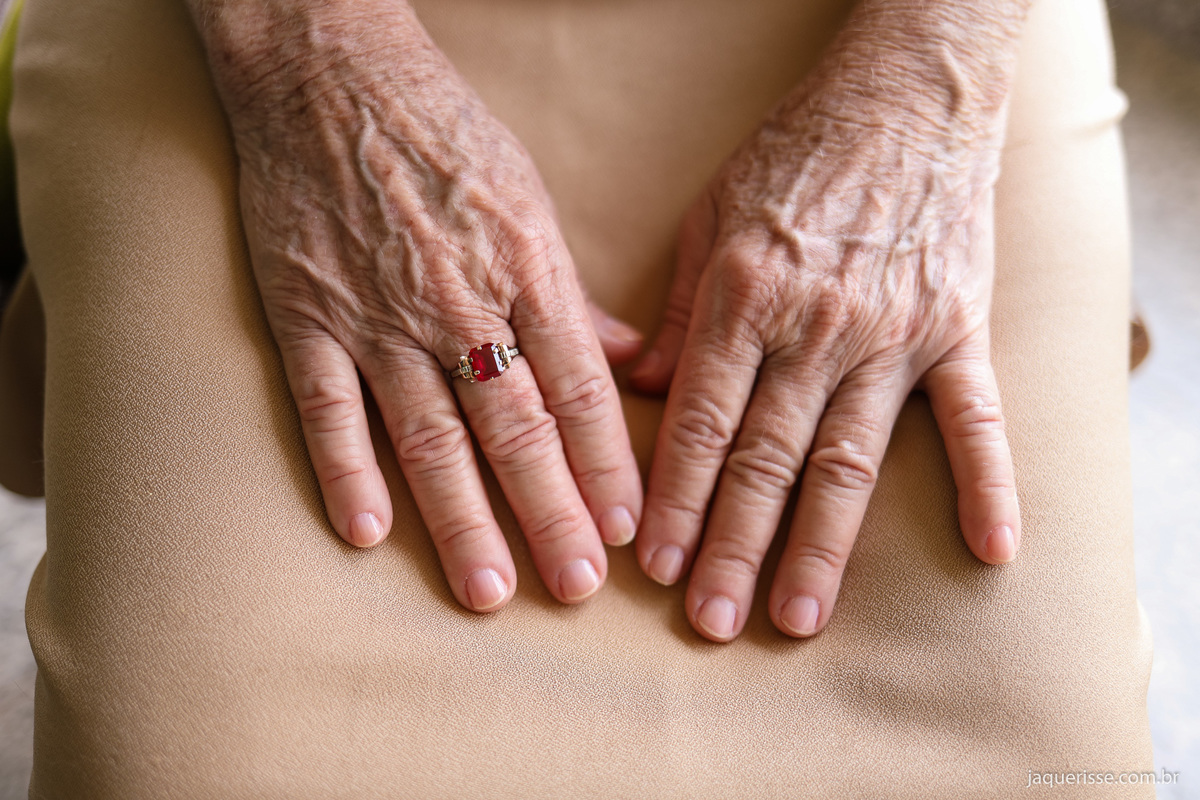 mãos da noiva sobre seu vestido mostrando o lindo anel vermelho que a noiva utilizou durante toda a cerimonia de bodas de ouro fotografado pela fotografa de casamentos jaque risse