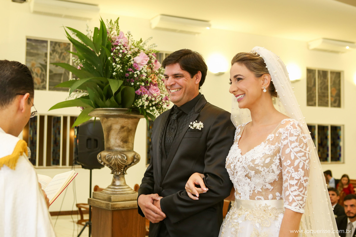 jaque risse, andre risse, estudio bebedouro, melhores fotografos, noivos no altar sorrindo, vaso de flores ao lado deles e o padre a frente