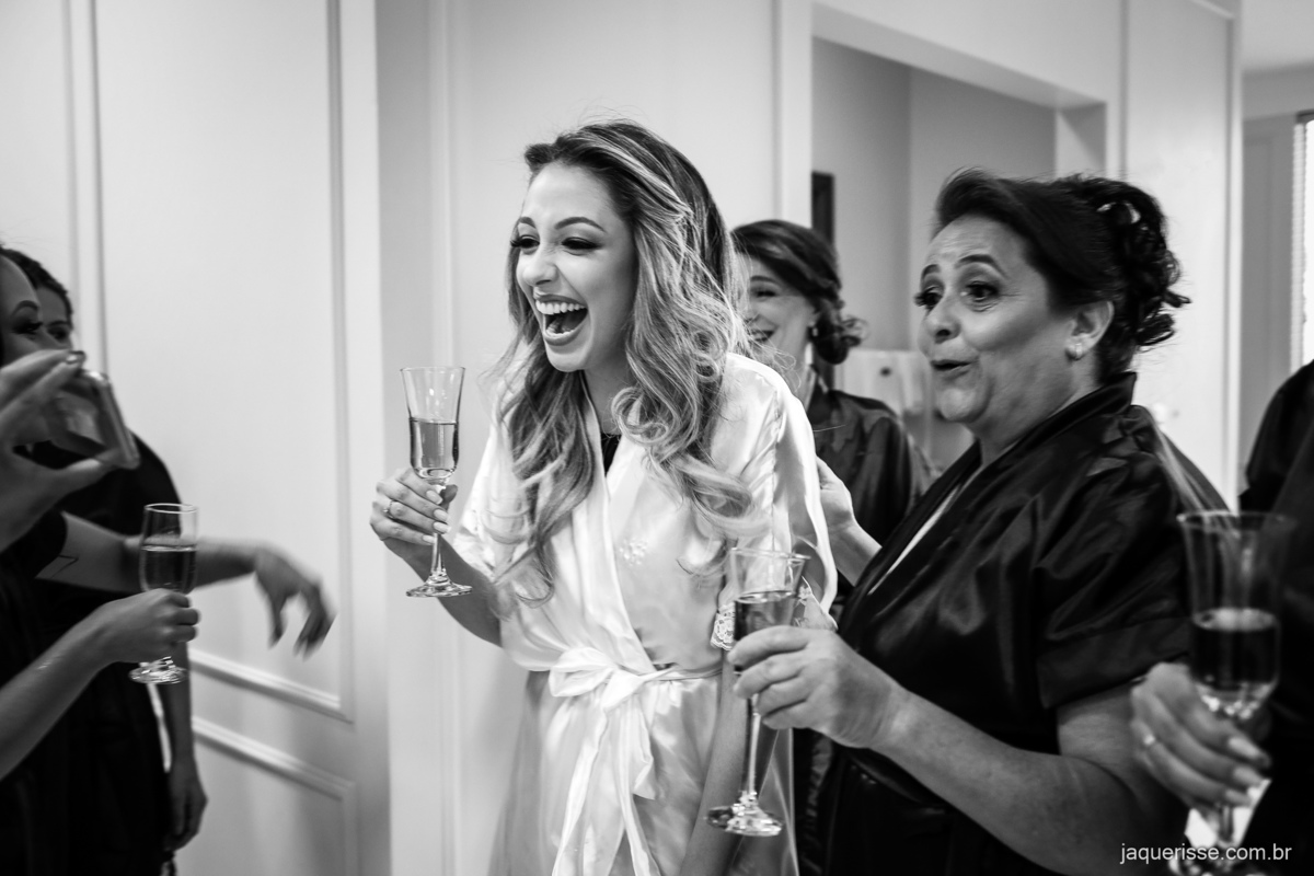 noiva segurando a taça de champanhe e sorrindo junto com sua mãe e madrinhas num momento de descontração durante o brinde registrado pela jaque risse em bebedouro sp