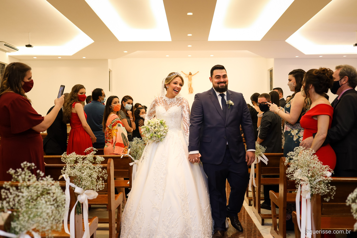 saída super sorridente e feliz dos noivos pelo corredor central da igreja recebendo os aplausos dos convidados fotografado pela jaque risse em bebedouro sp