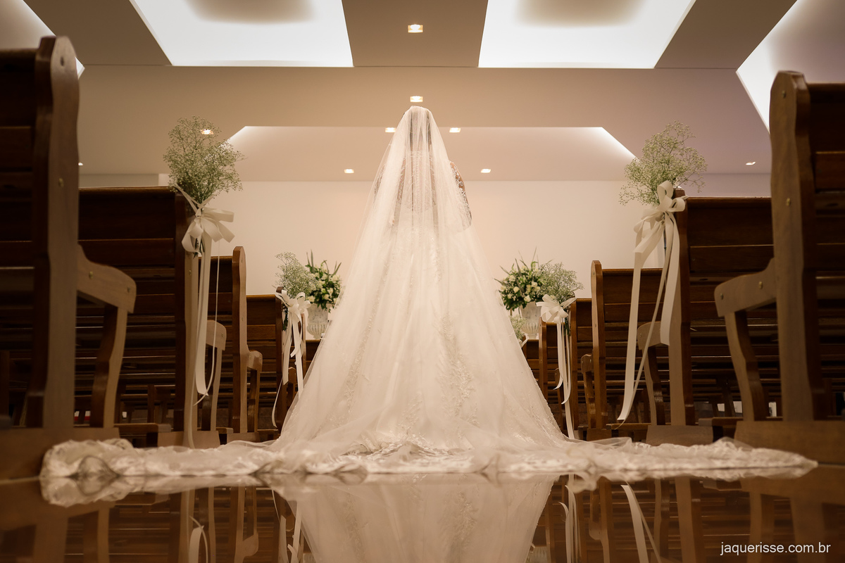 noiva de costas com seu longo vestido branco bem ao centro do corredor da igreja vazia fotografado pela jaque risse em bebedouro sp