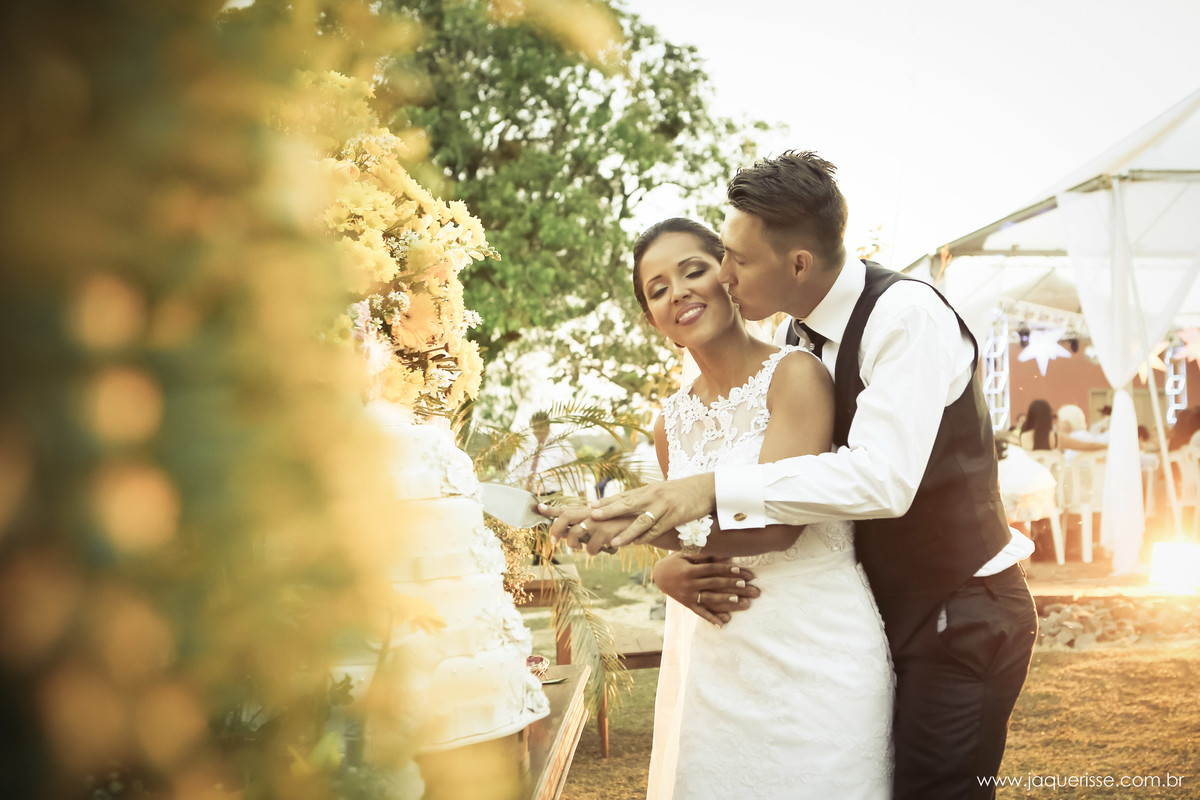jaque risse, andre risse, estudio bebedouro, melhores fotografos, noivo beijando a bochecha da noiva, a noiva de olhos fechados sorrindo, e ambos cortando o bolo