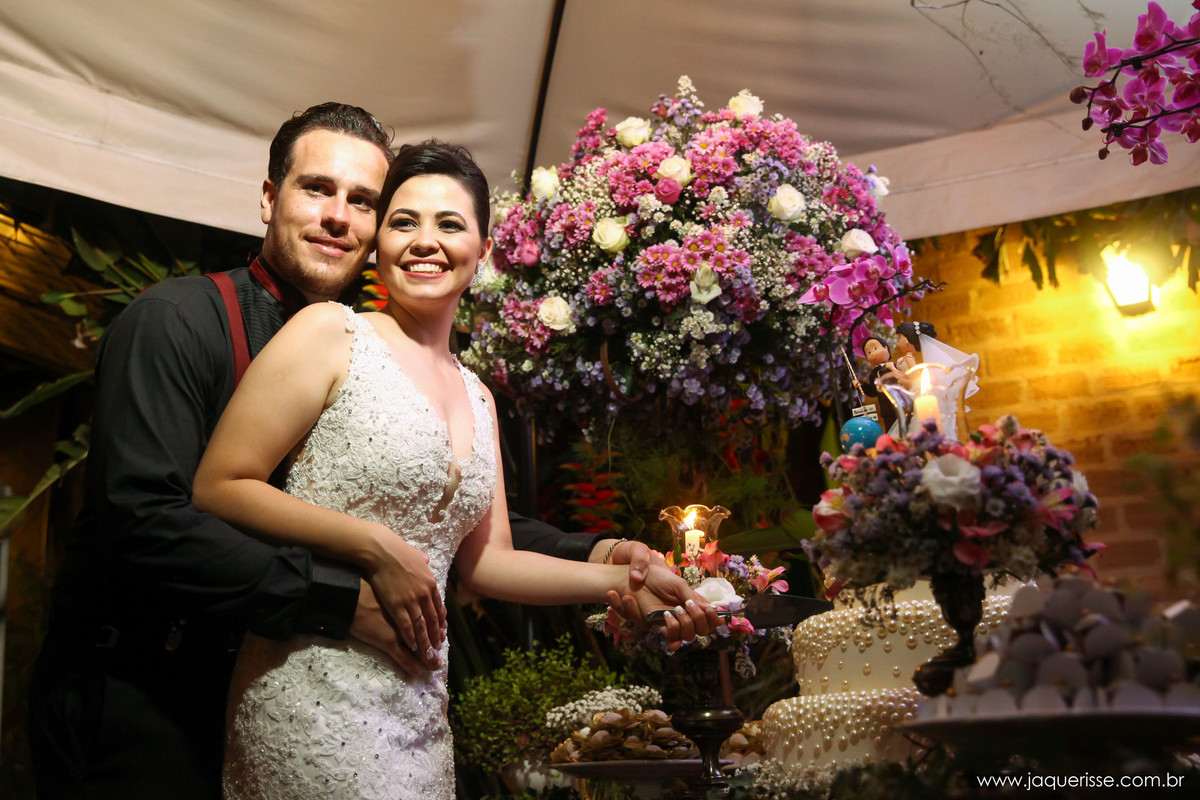 jaque risse, andre risse, estudio bebedouro, melhores fotografos, decoraçao atras dos noivos, bolo e doces na mesa, noivos cortando o bolo com um enorme sorriso em seus rostos