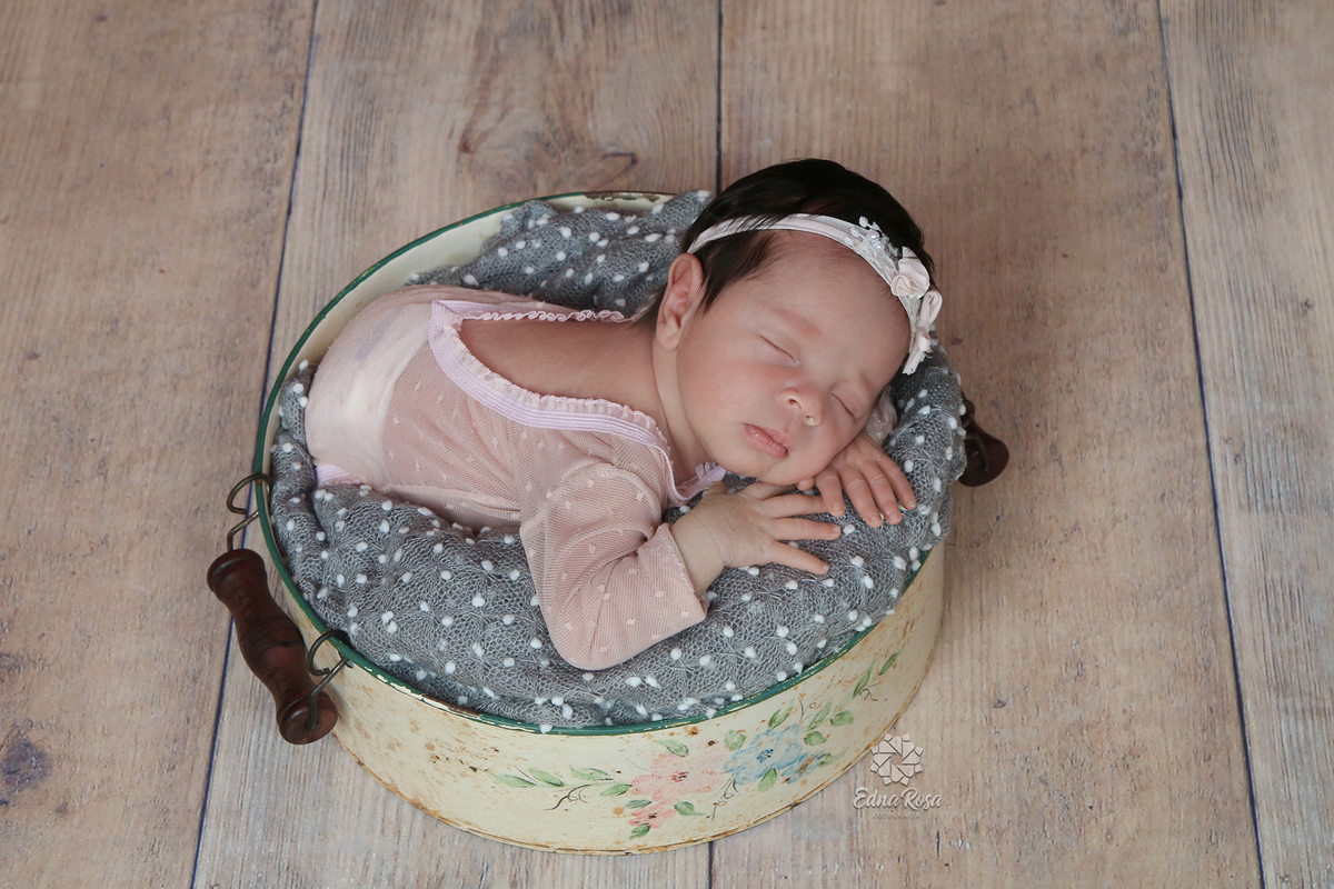 Foto da bebê usando body em renda branco e posicionada dentro de um prop. 