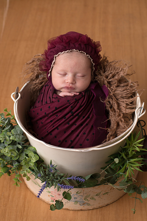 Foto do recém nascido dentro do balde usando wrep e toquinha na cor vinho