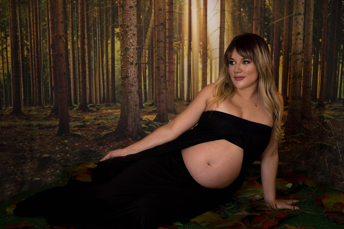 Fotografia de gestante no estúdio edna rosa fotografia. Gravida usando saia e top preto. Está sentada apoiando corpo sobre o braço