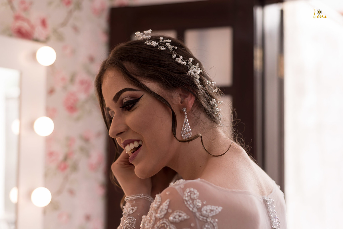 noiva sorrindo e colocando brinco em frente ao espelho