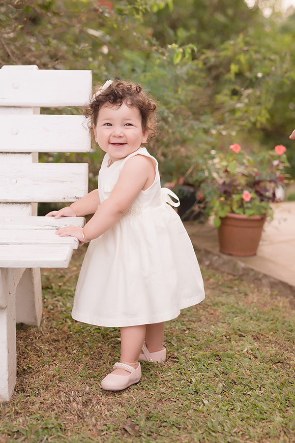 fotografia infantil em caxias do sul 
 menina de vestido branco encostada no banco de madeira sorrindo  em Caxias do Sul