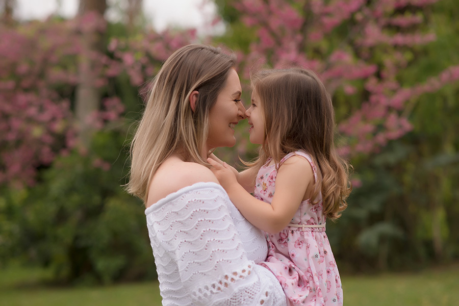 fotografia gestante em caxias do sul; Morgana Perini; Fotografia de família em Caxias do Sul; Mãe segurando filha no colo com árvores em flor