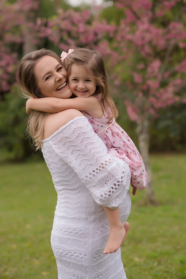 fotografia gestante em caxias do sul; Morgana Perini; Fotografia de família em Caxias do Sul; Mãe abraçando a filha com árvores em flor