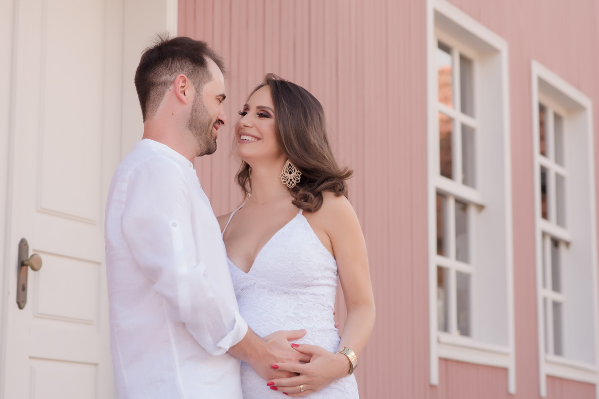 foto gestante em caxias do sul fotografa morgana perini casal de branco em frente a uma casa rosa