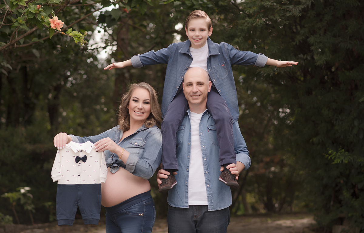 foto de gestante em caxias do sul fotografa morgana perini familia segurando a roupinha do novo integrante