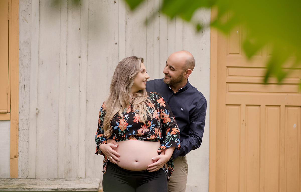 foto de gestante em caxias do sul fotografa morgana perini casal abraçado proximo a casa de madeira