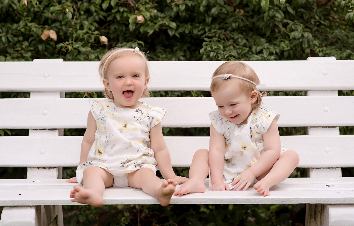 foto de gemeas em caxias do sul fotografa morgana perini bebes sentada em banco branco em jardim