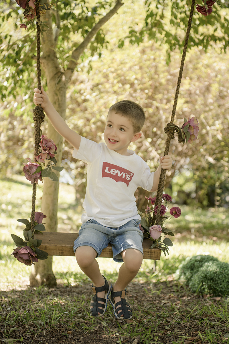 Foto criança em caxias do sul fotografa morgana perini menenino balanço sorrindo flores