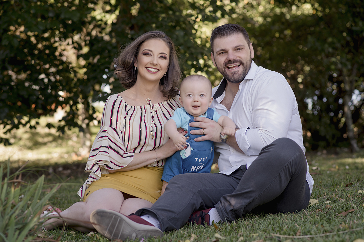 Foto de bebe em caxias do sul fotografa morgana perini casal sorrindo com filho sentados na grama