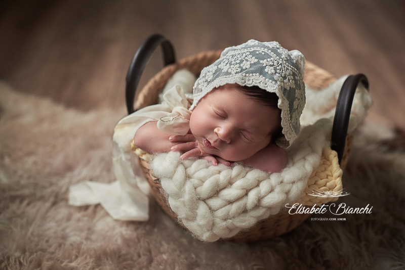 Foto de recém-nascida japinha em ensaio newborn, dormindo dentro do cesto, de bruços, apoiada nos bracinhos, e com touquinha rendada, realizada na residência dos pais, em Caxias do Sul - RS.