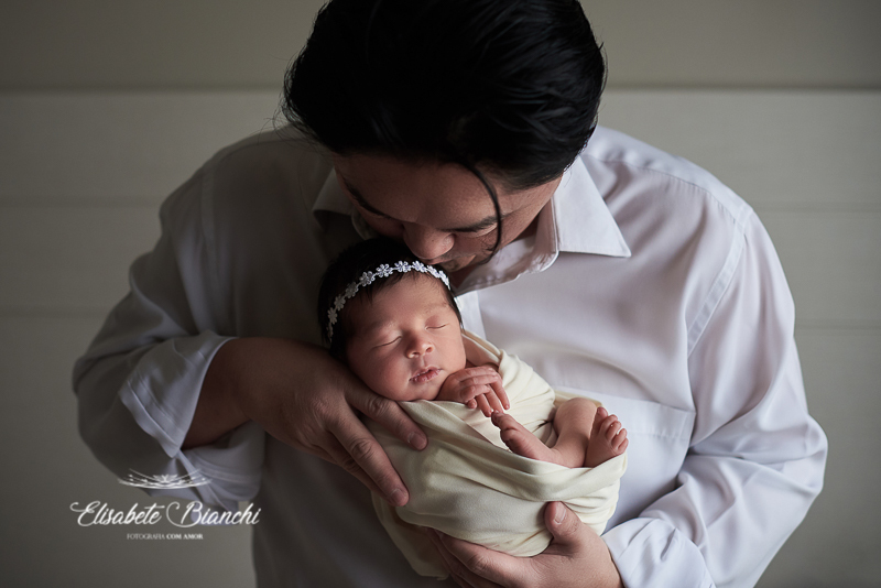 Pai japonês beijando filha recém-nascida em ensaio newborn. As fotos foram realizadas no domicílio, em Caxias do Sul - RS.