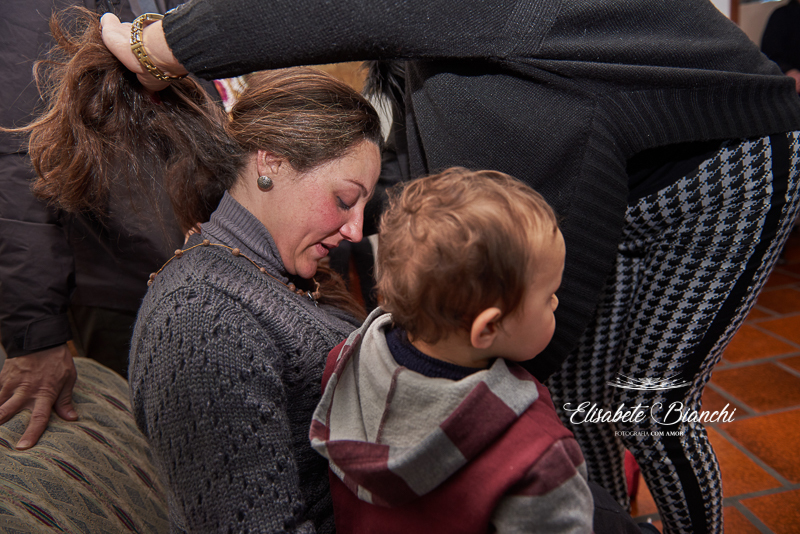 Gestante com seu filho mais velho no colo, recebendo de sua mãe o colar de contas com as intenções para seu bebê que está para nascer, realizado por familiares e amigos, no chá de bênçãos, em Caxias do Sul.