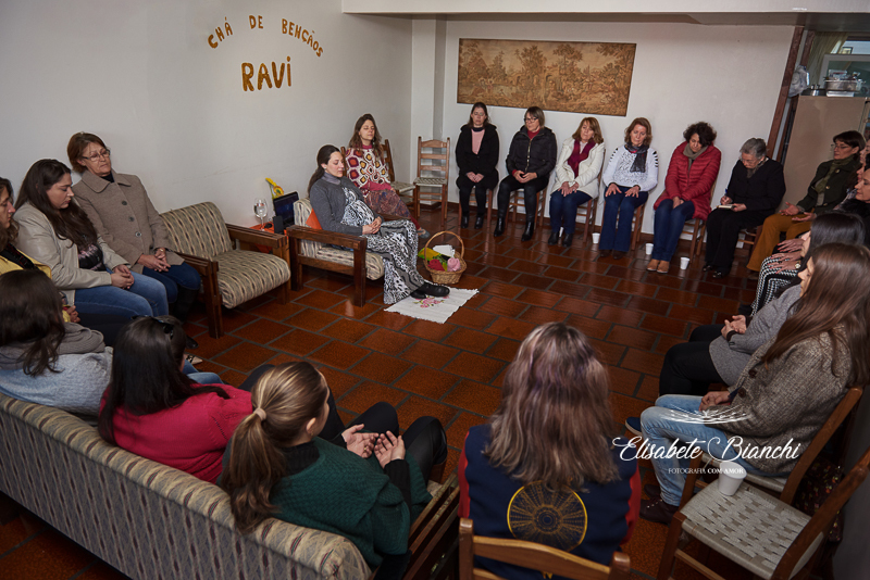 Grupo de mulheres reunidas em torno de gestante, em chá de bênçãos, em Caxias do Sul.